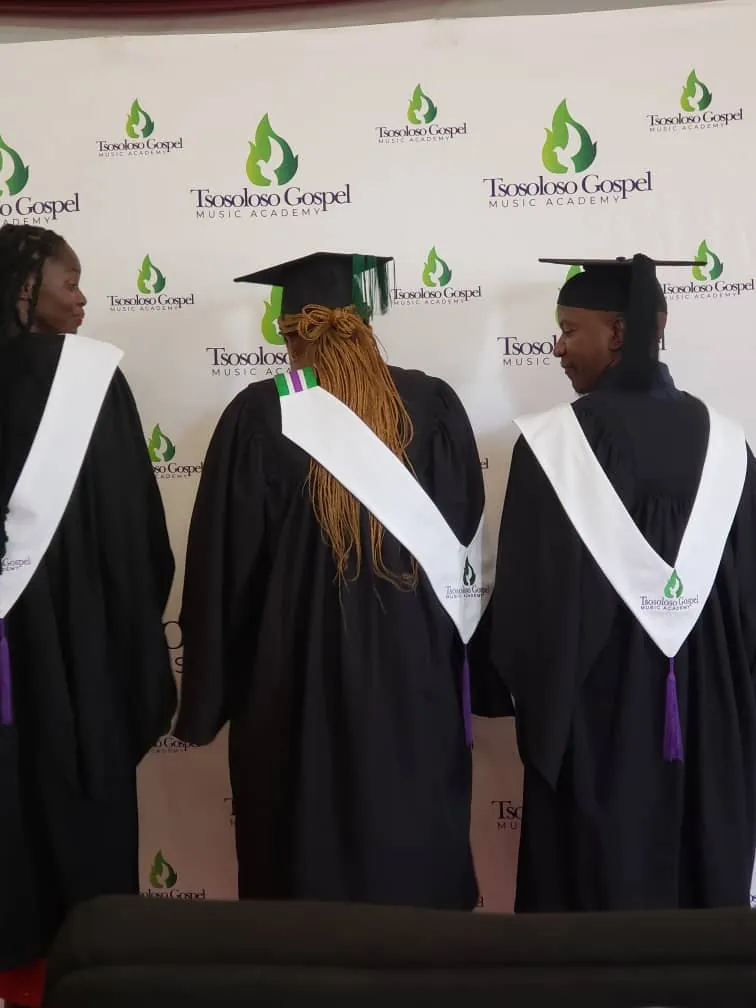 TGMA graduates in academic gowns standing before the Tsosoloso Gospel Music Academy branded backdrop